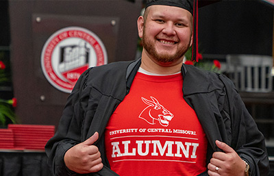 Thumbnail image: A UCM alum showing their alumni shirt at Commencement